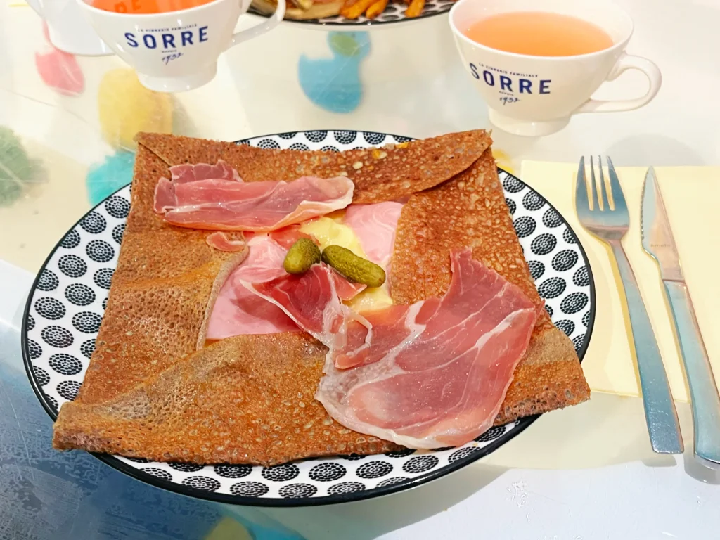 Galette Pépé Robert au fromage à raclette, emmental, jambon cru et pommes de terre, avec deux tasses de cidre.